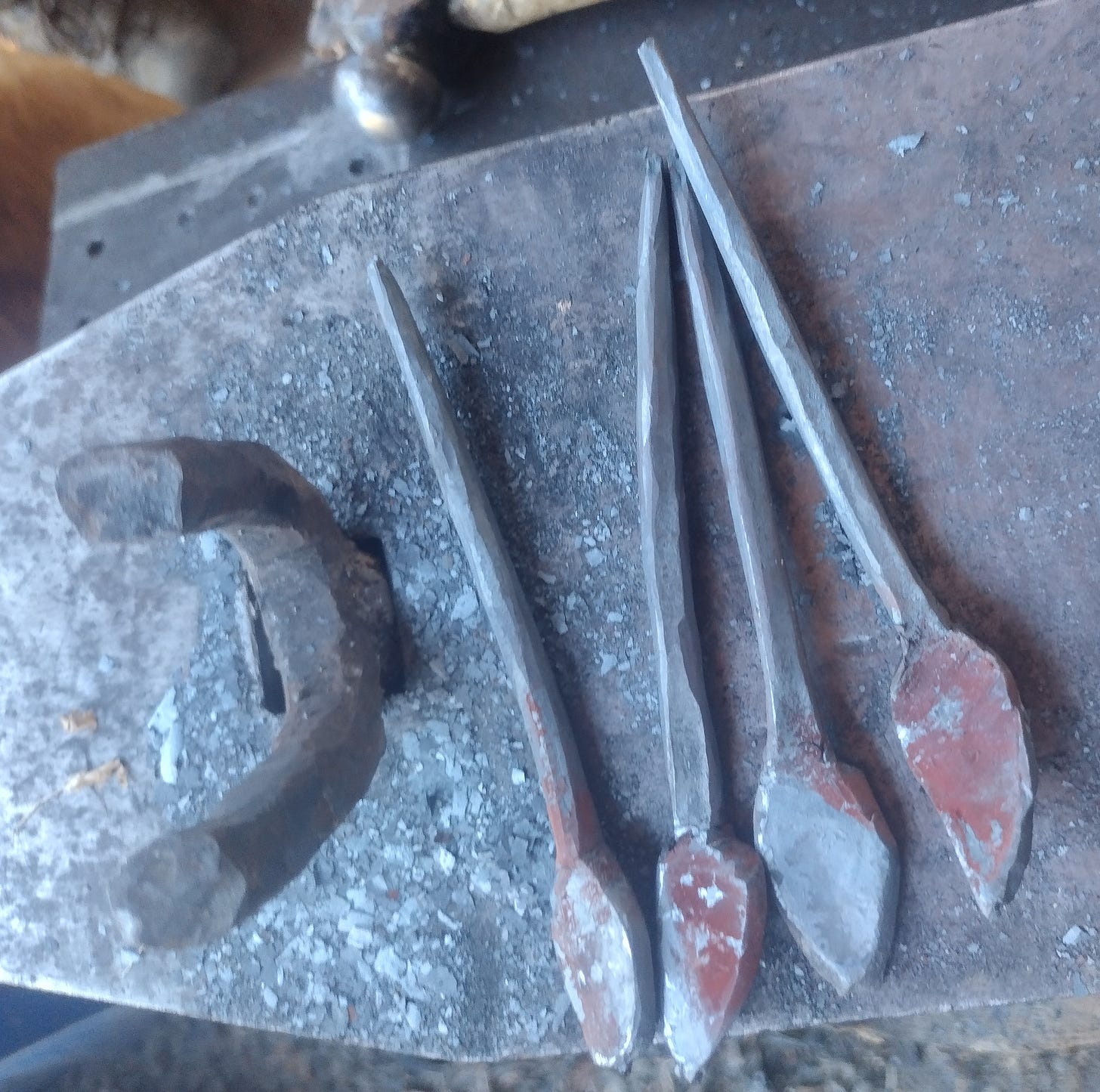 Anvil populated by four half-made hooks with spade finials.