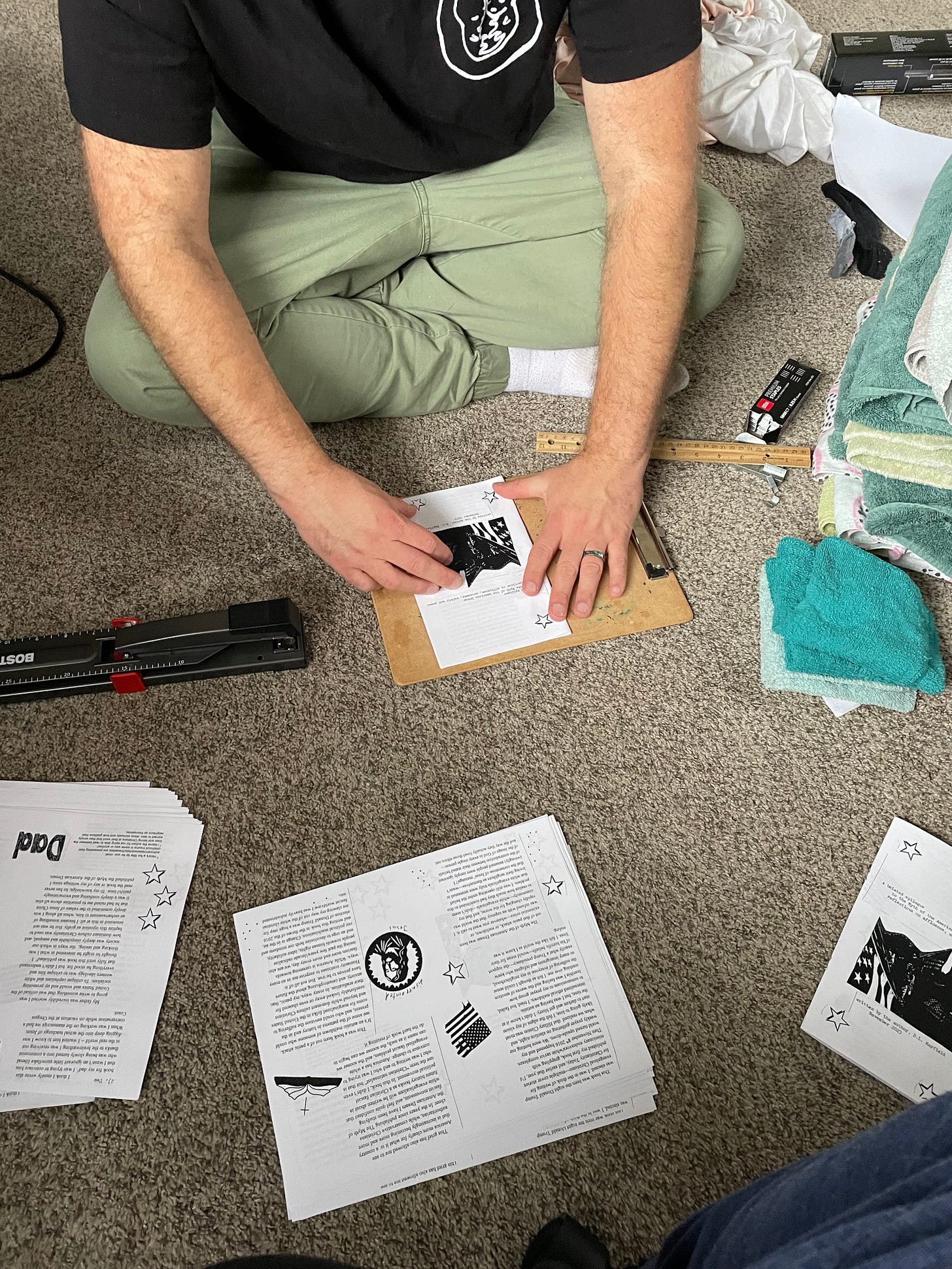 a white man is sitting cross-legged n the floor and he is folding zines