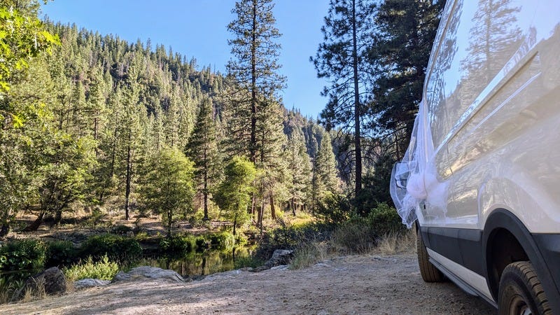 A nice camping spot by the river with clear blue sky, the side of the van, and no smoke in sight