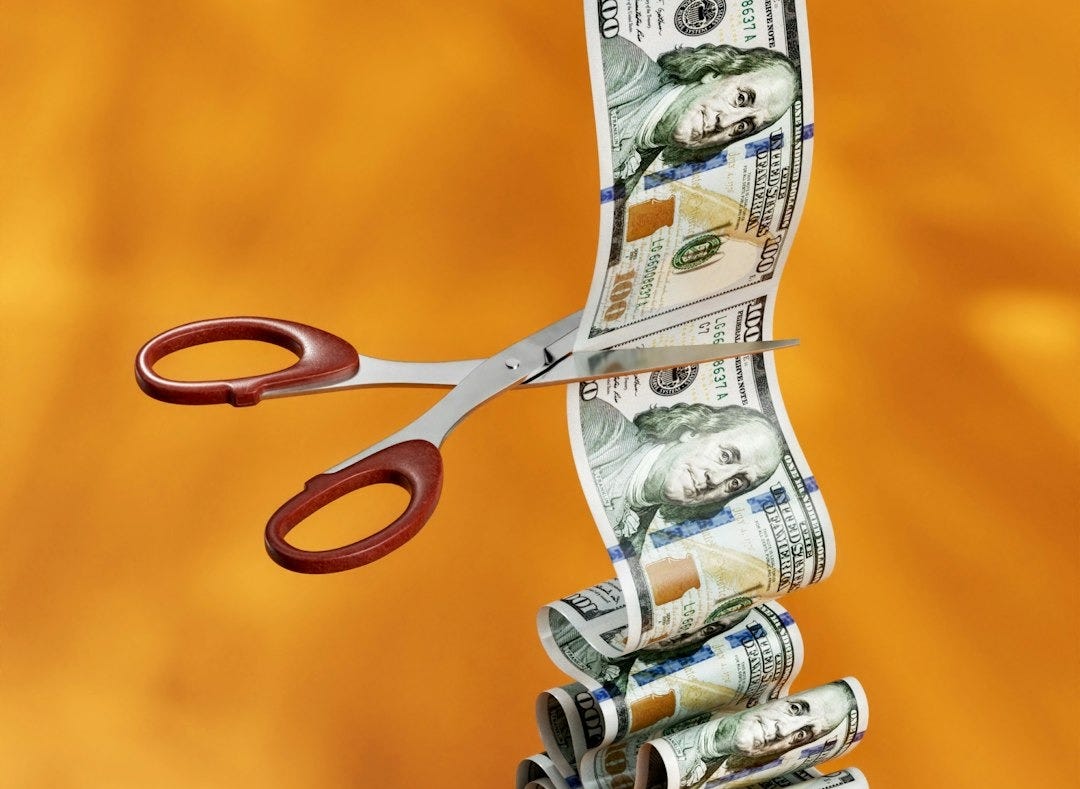 a stack of money sitting next to a pair of scissors a stack of money sitting next to a pair of scissors