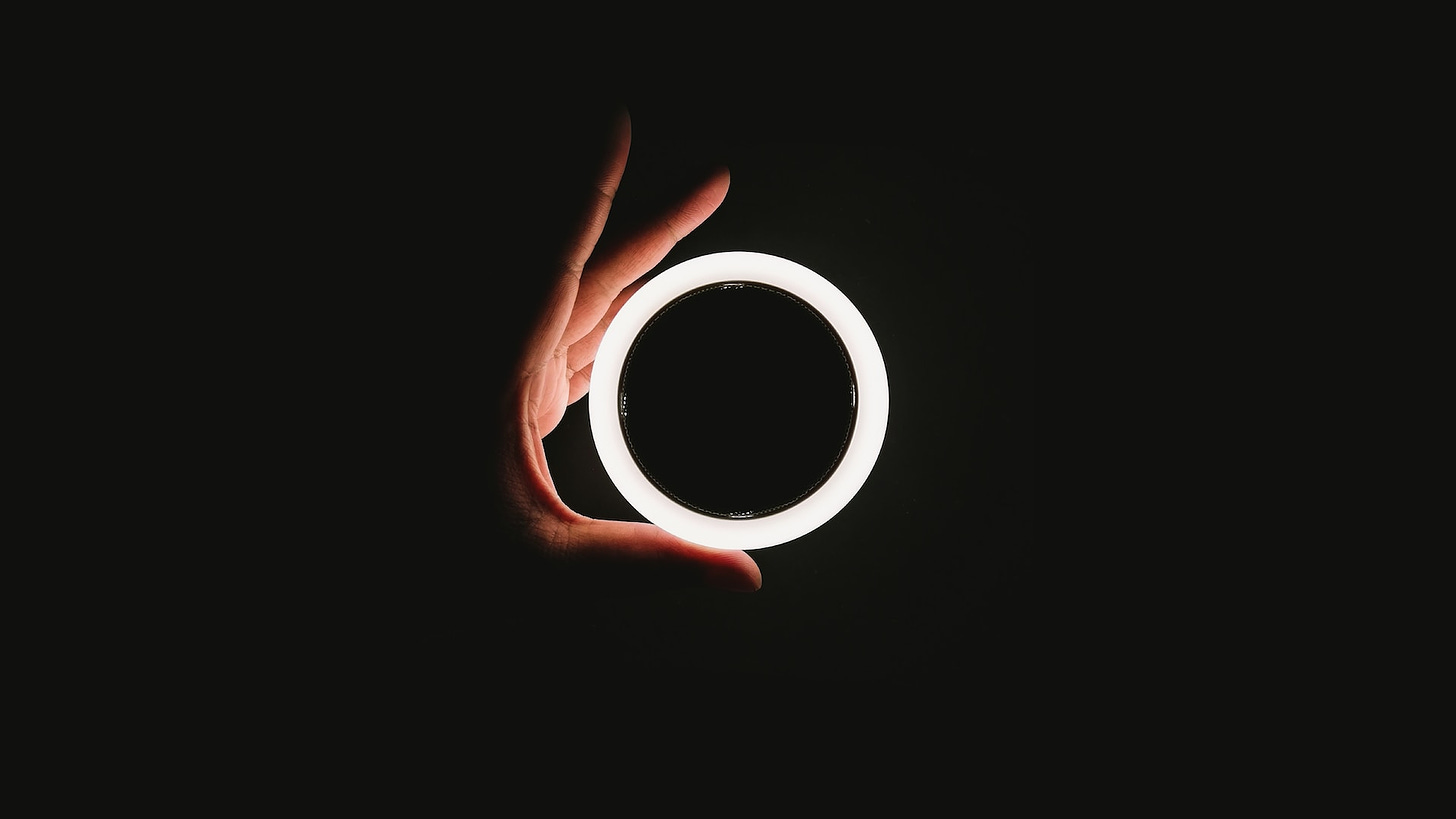Sfondo nero con una mano che compare di profilo a sorreggere un anello luminoso di color bianco.