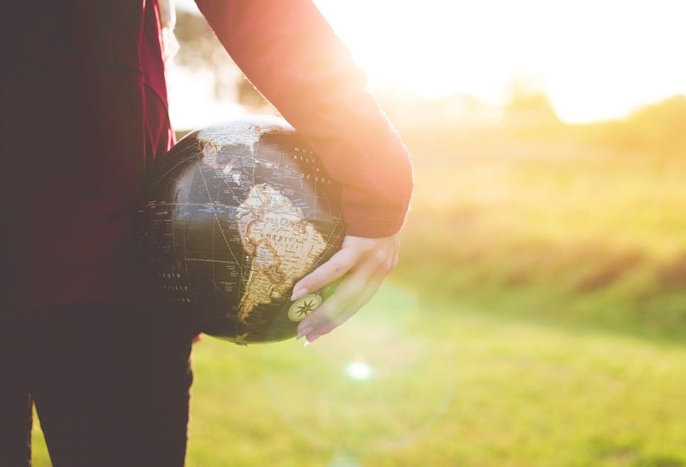 person holding black and brown globe ball while standing on grass land golden hour photography