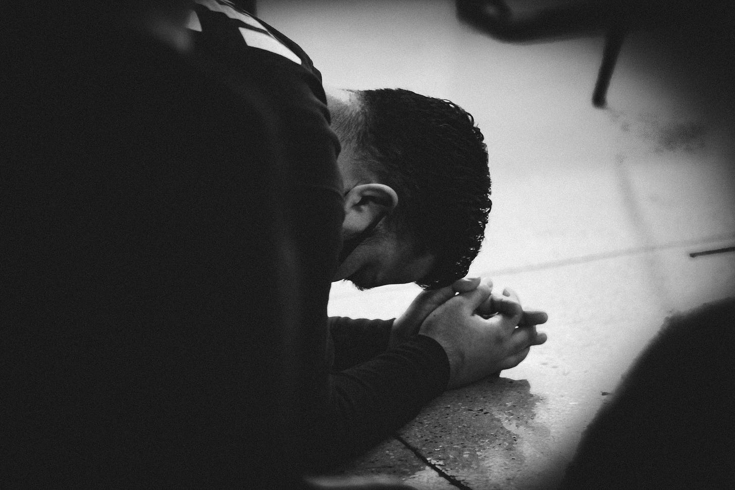 B&W image of a young man bowing on the floor, hands folded in prayer.