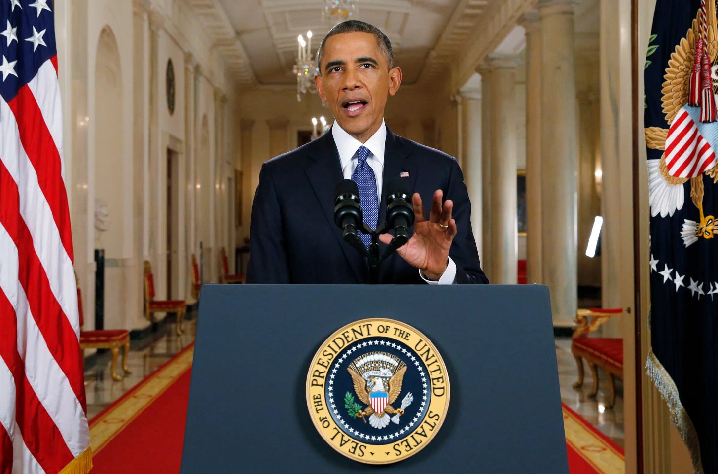 This image shows a photo of United States President Barack Obama, in a 19 Febraury 2016 photo, standing at a podium bearing the presidential seal and located in the White House's Cross Hall. This image shows a photo of United States President Barack Obama, in a 19 Febraury 2016 photo, standing at a podium bearing the presidential seal and located in the White House's Cross Hall.