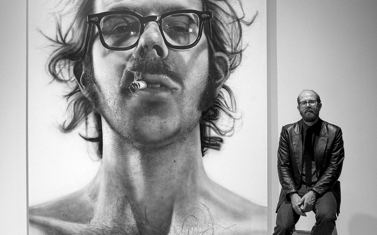 Man sitting on stool in front of large portrait of man wearing glasses with cigarette in mouth