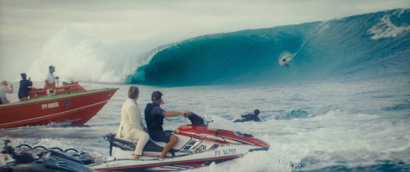 A surfer rides a huge wave as people in speedboats look on.