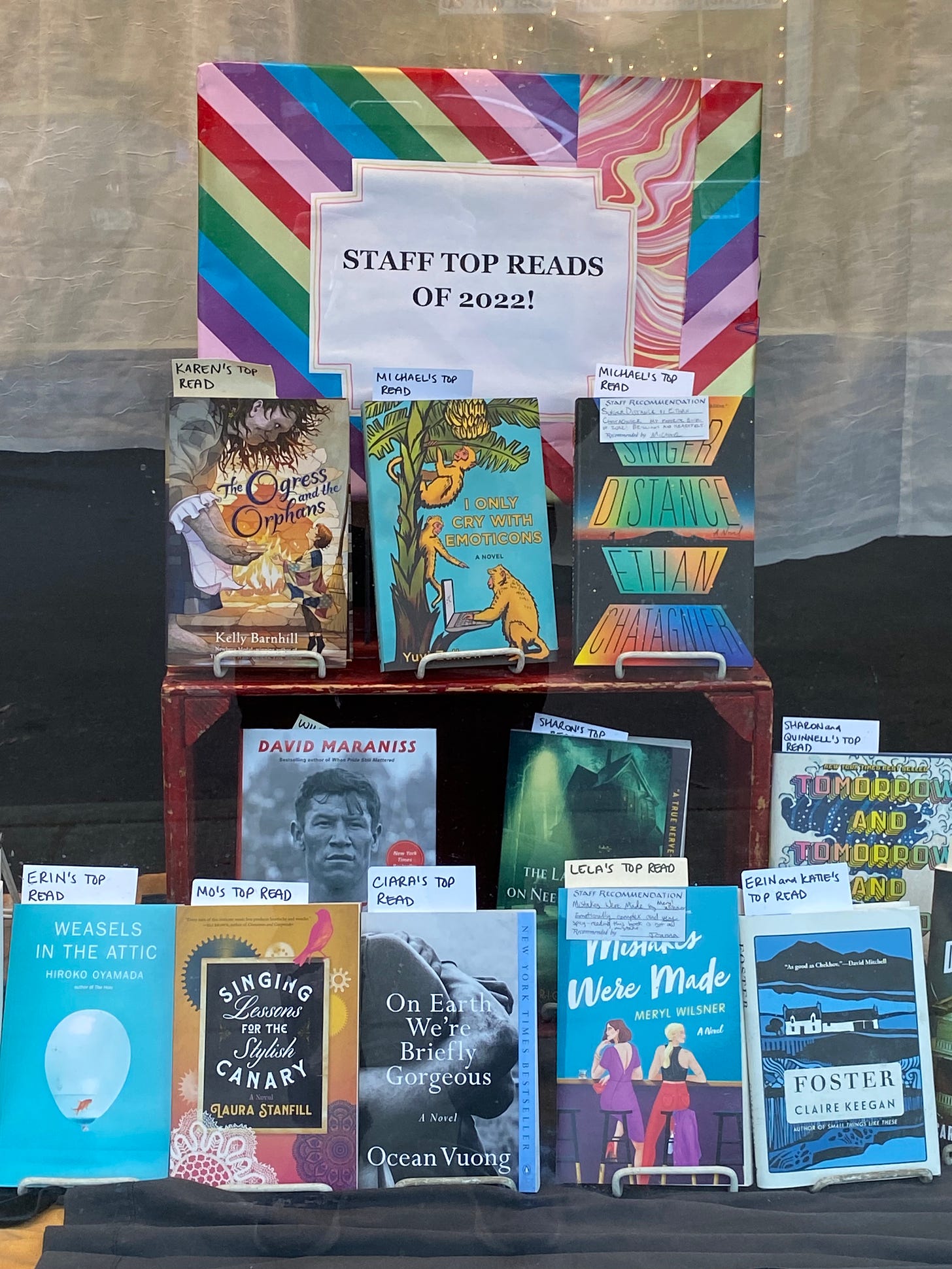 Books in a store window, with a sign that says STAFF TOP READS of 2022. Singing Lessons for the Stylish Canary is in the center-left of the photo. 