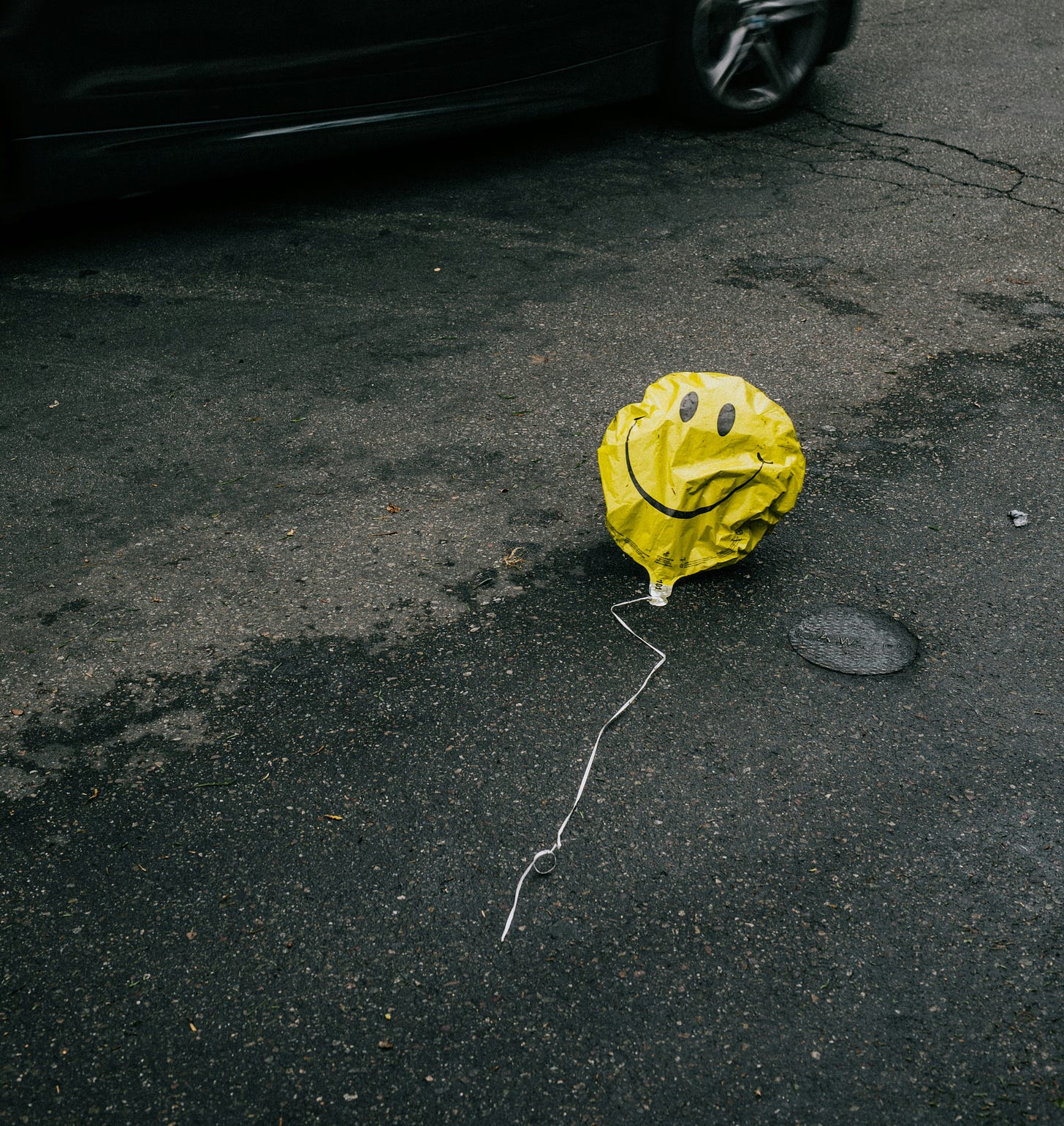 A half-deflated yellow balloon with a smiley face lying on the road.