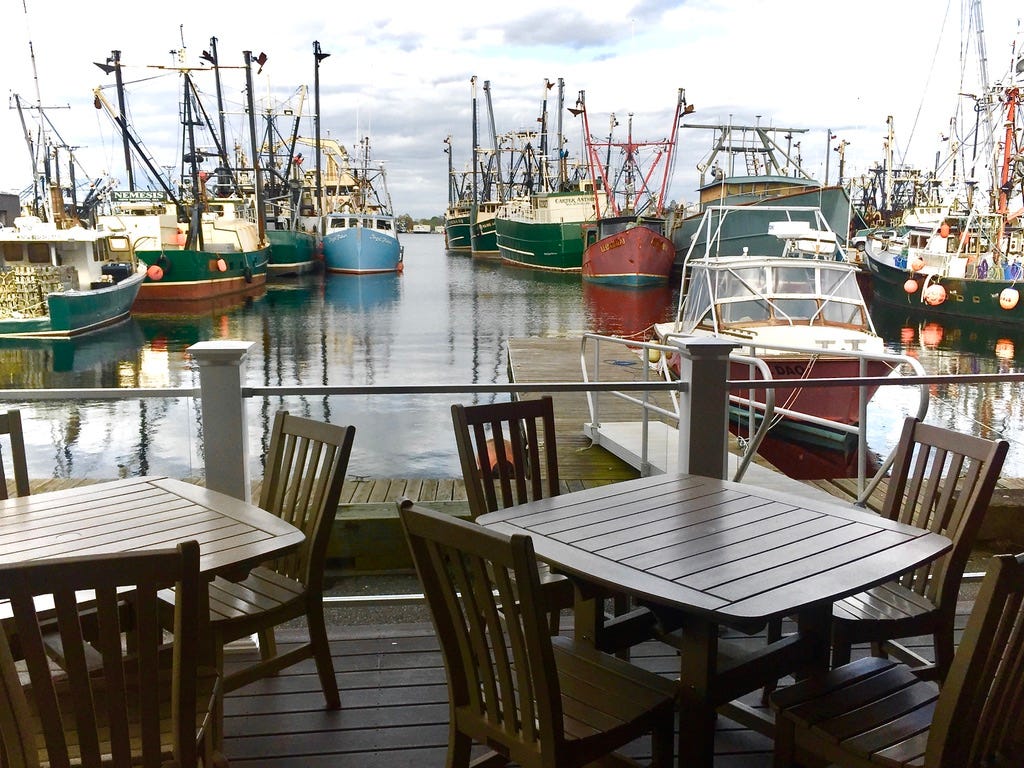 A table and chairs on a dock with boats in the background

Description automatically generated