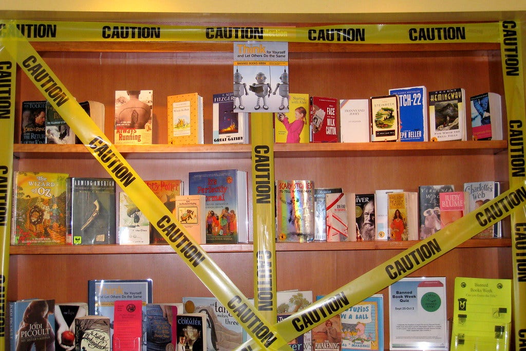shelves of books that have been banned with caution tape wrapped around