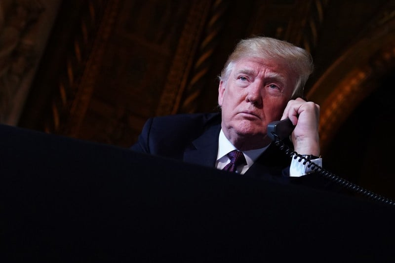 Donald Trump wearing a suit and tie looks up as he talks on a corded phone.