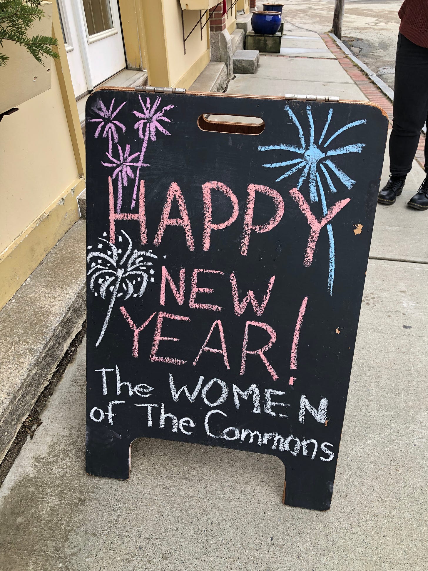 A sandwich board sign reads Happy New Year! The Women of The Commons, written in chalk