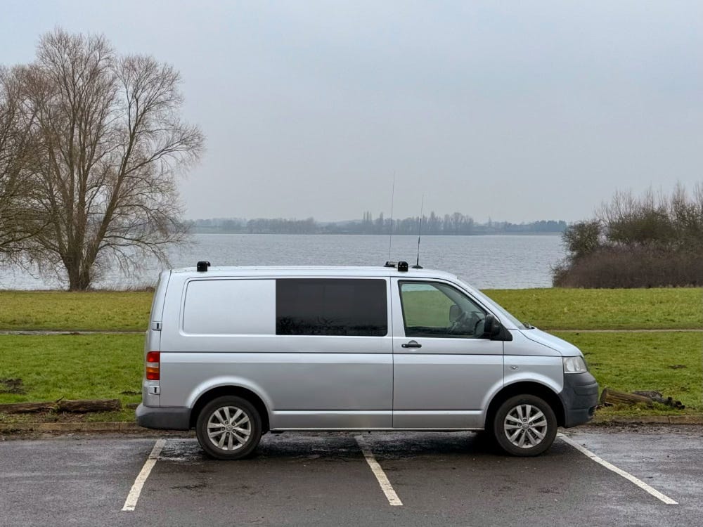 A 2009 VW transporter T5 sits parked on the edge of a carpark overlooking a reservoir.