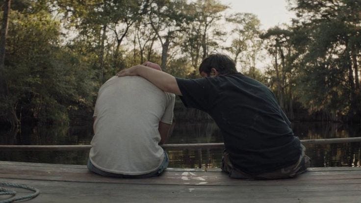 This may contain: two people sitting on a dock looking at the water