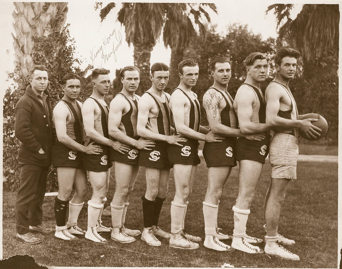 A line of men in shorts and athletic shirts with palm trees in the background