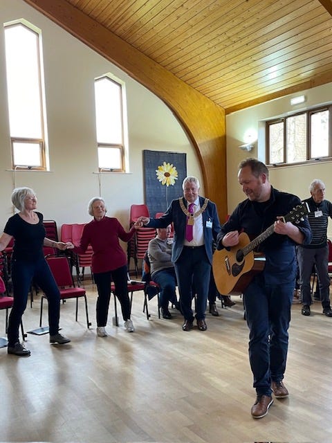 Ryan Dixon leading a singing session playing the guitar, the group in the background includes Blackburn mayor