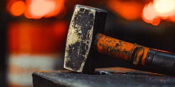 a hammer on an anvil, blurred fire behind.