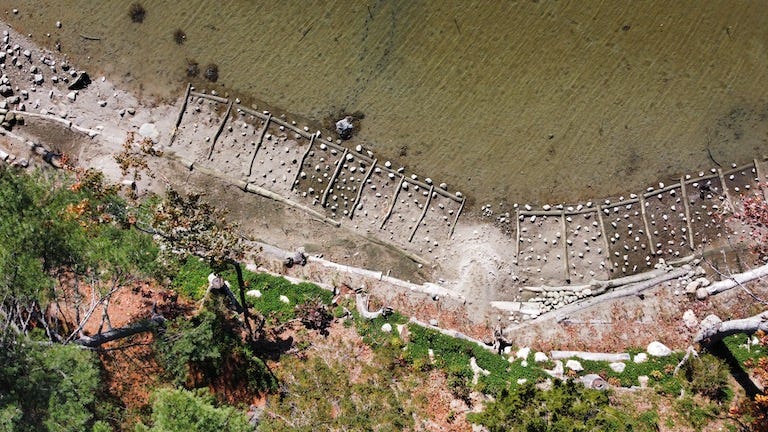 Drone image of the erodible bluff (bottom) being stabilized by tiers of logs pinned to the ground, back-filled with soil, and planted among erosion-slowing rocks to keep the rising waters at bay, for a 'living shorelines' project on the Blue Hill Peninsula in Maine. Image by Erik Hoffner for Mongabay.
