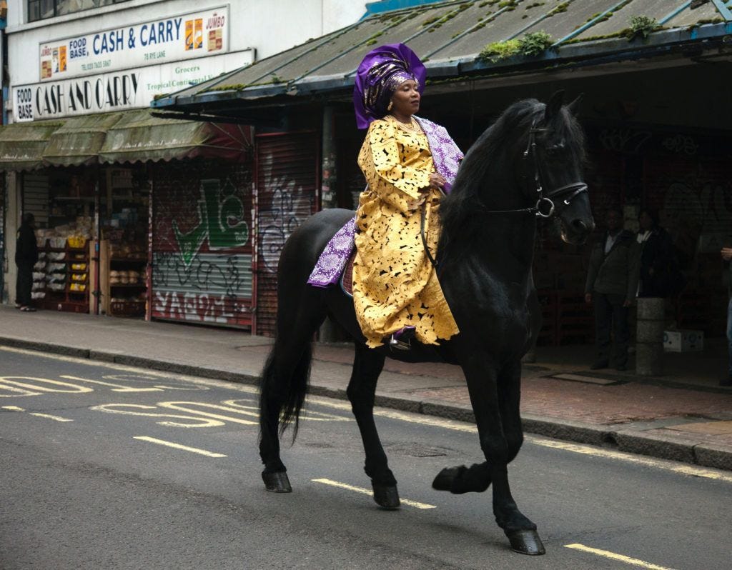 Still from a short film called “Entitled” directed by Adeyemi Michael showing a Black African woman in traditional Nigerian dress rides a horse down Rye Lane, a street in South London known for its large African and Caribbean communities.