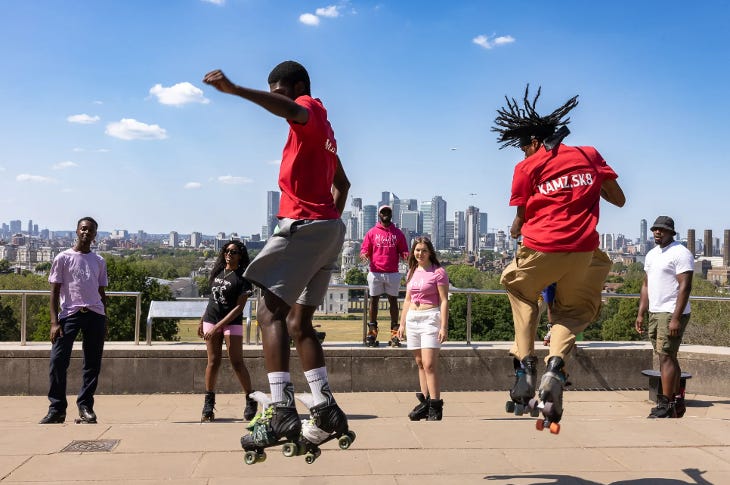 Expert roller skaters performing tricks in Greenwich Park, with spectators watching them