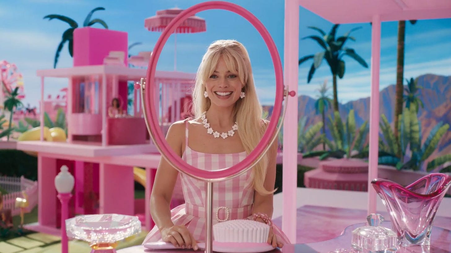 Movie still from Barbie. Barbie smiles at a mirror that has no glass, only a frame.