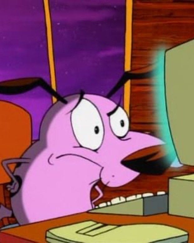 Courage the Cowardly Dog, an animated purple dog character, sits with his front paws on his hips as he looks at a lit-up desktop computer screen. The screen is glowing blue. His expression implies confusion and frustration at what he is seeing on the screen.