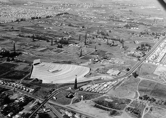 Aerial view of Torrance in the 1950s, looking down on a drive in movie theater and dozens of oil derricks.
