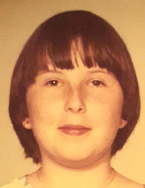 Junior high aged girl with dark bob and bangs, round face, dark eyes, and a bit of a Mona Lisa smile.