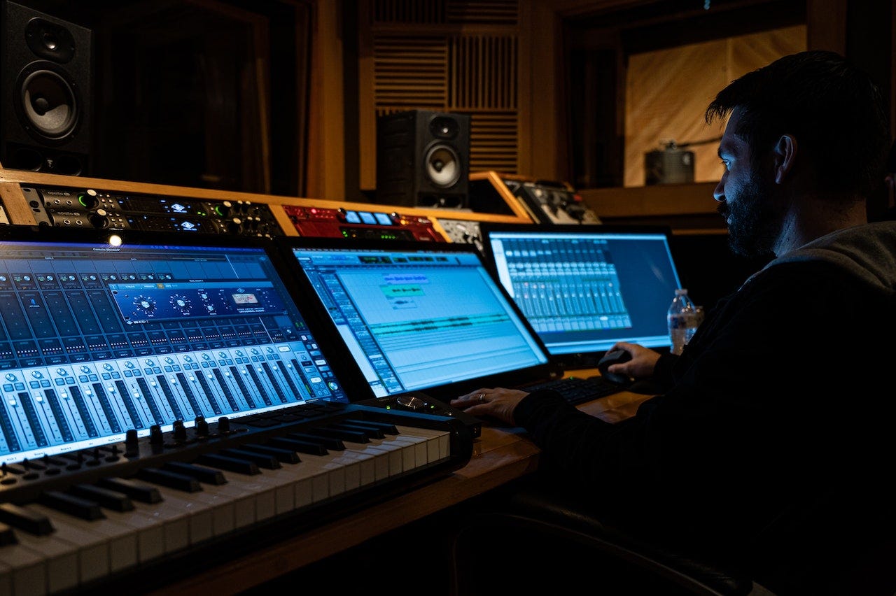 A bearded man sits at mixing desk in a professional studio. In this example, he is working on music rather than a film mix.