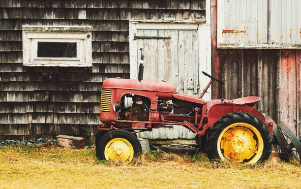 Vintage Farming A 1940's era tractor beside a neglected barn. rusty farm equipment stock pictures, royalty-free photos & images