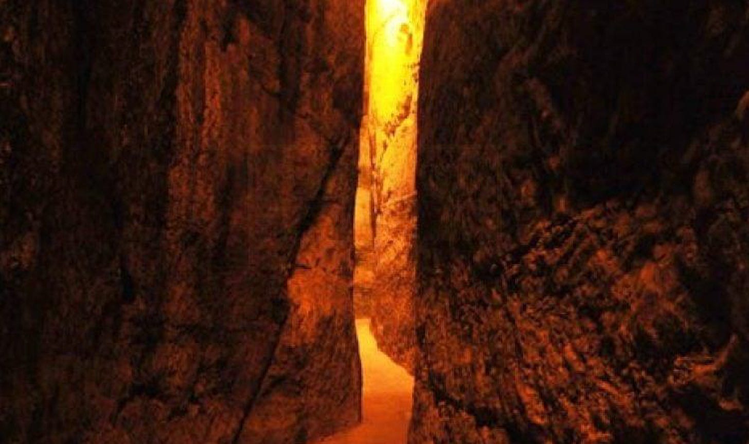 Dark, narrow passage between stone walls with light ahead