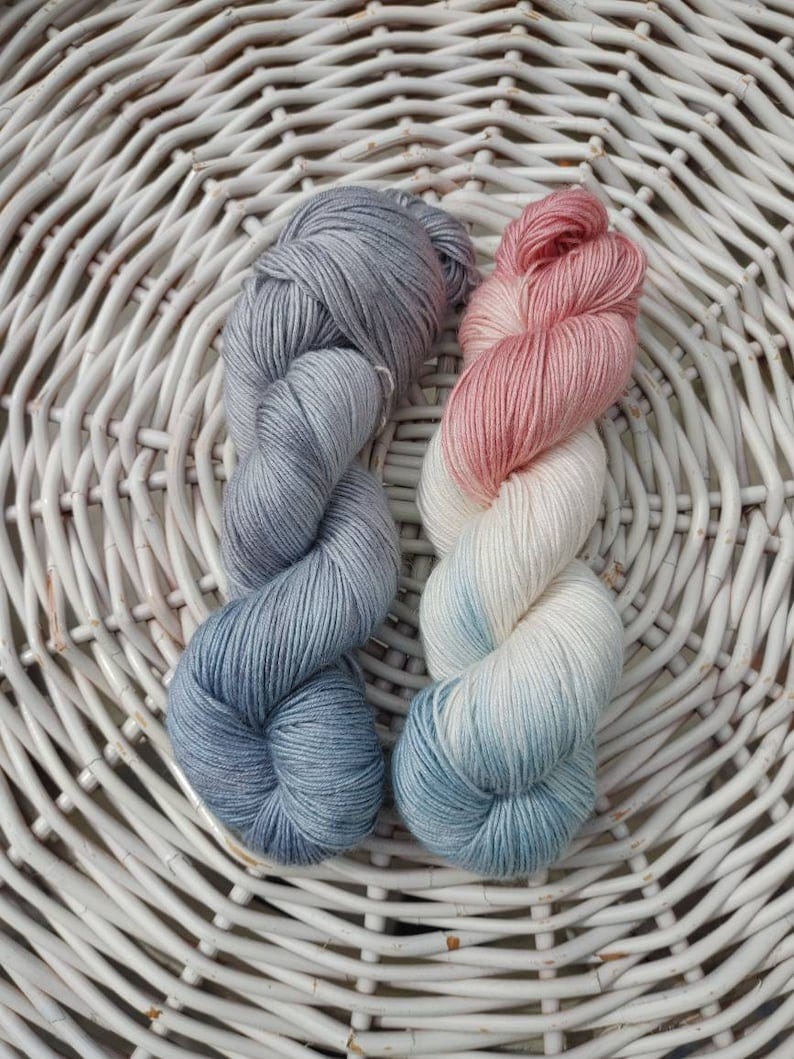May include: Two skeins of yarn, one is a light blue color with a white gradient and the other is a pink color with a white gradient.