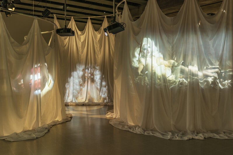 A series of white sheets hanging from the ceiling with videos of body projected onto them