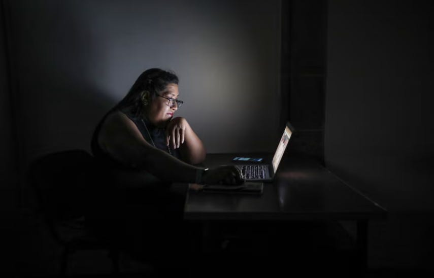 Side-on view of a Mexican woman using a laptop in a dark room.