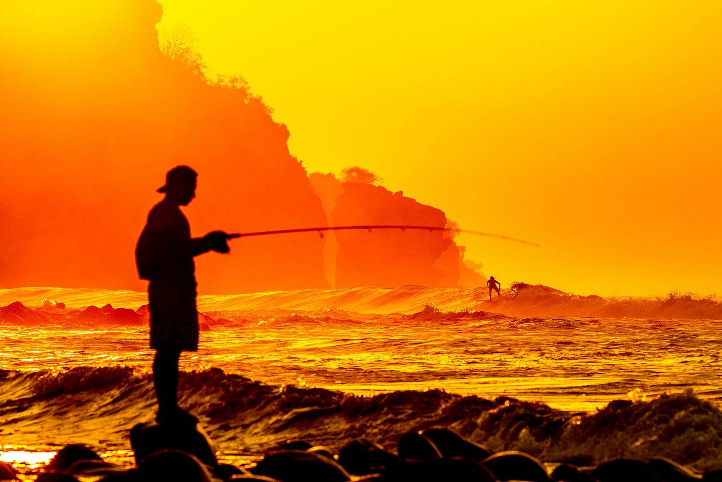 Silhouette of a man fishing at the beach during sunset