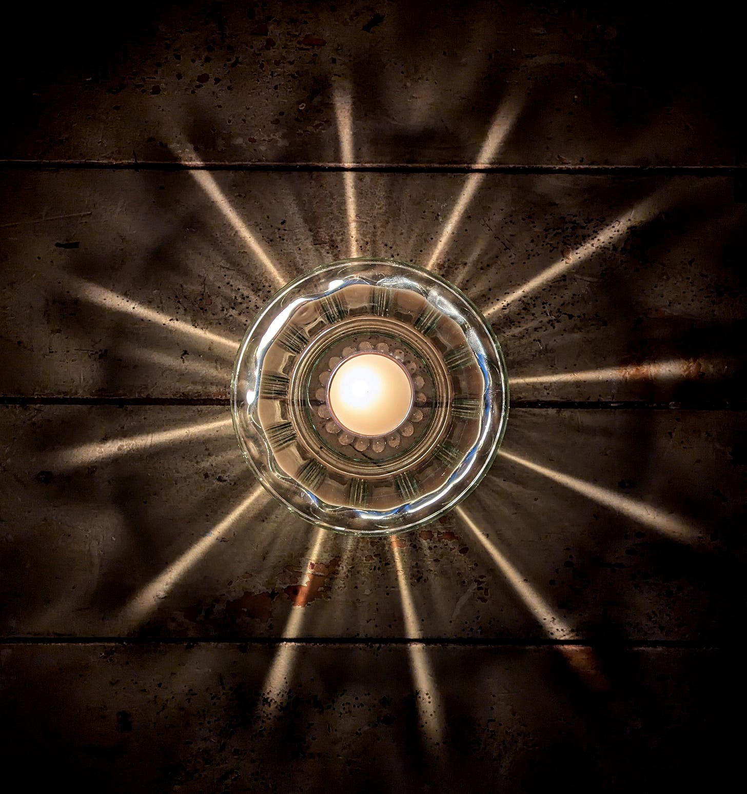 A beeswax tealight in a lined seafoam tinted glass dish, reflecting rays on a wooden table in the shape of a sun. A beeswax tealight in a lined seafoam tinted glass dish, reflecting rays on a wooden table in the shape of a sun.