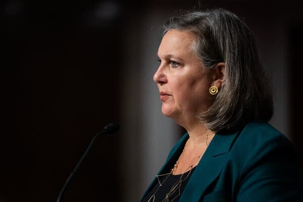 Victoria Nuland, in a dark top and dark green jacket, facing a microphone.