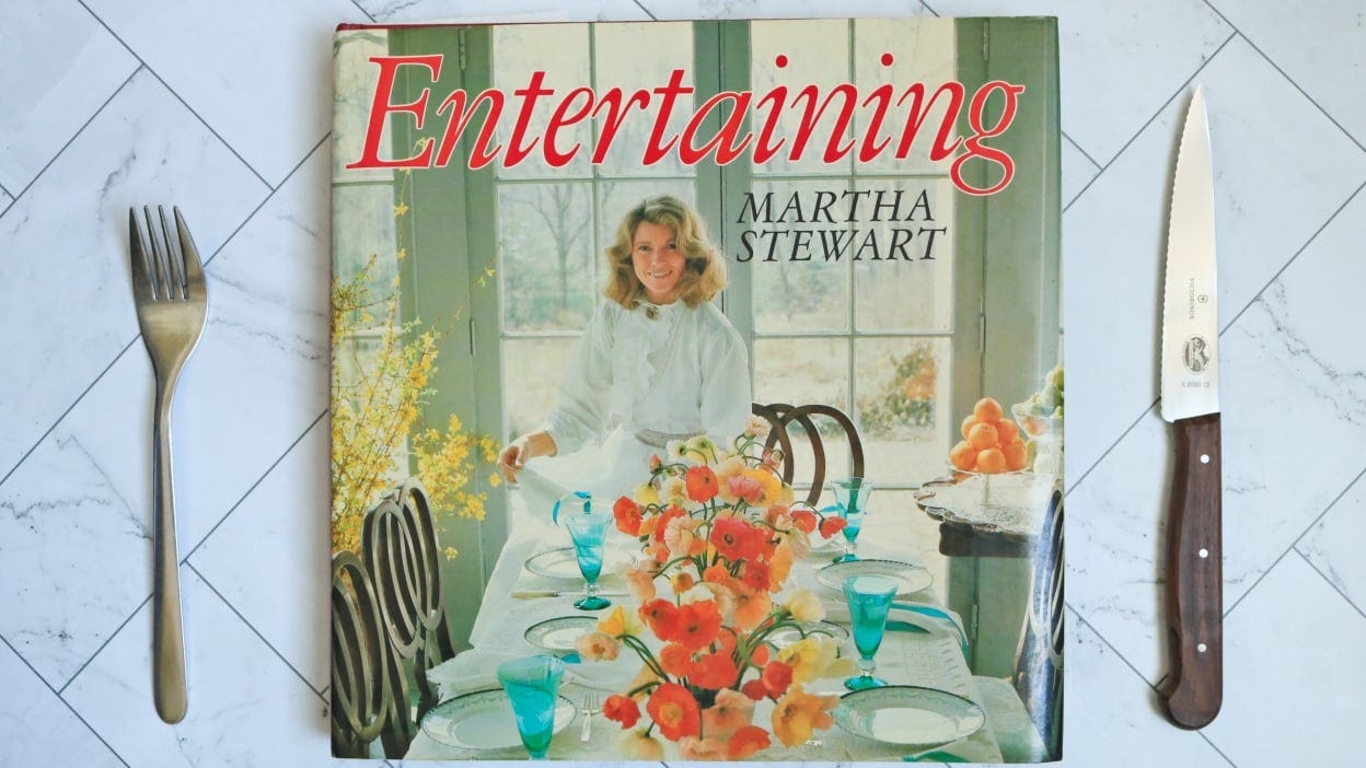 Martha Stewar's cookbook, Entertaining, on a counter with a fork and knife.