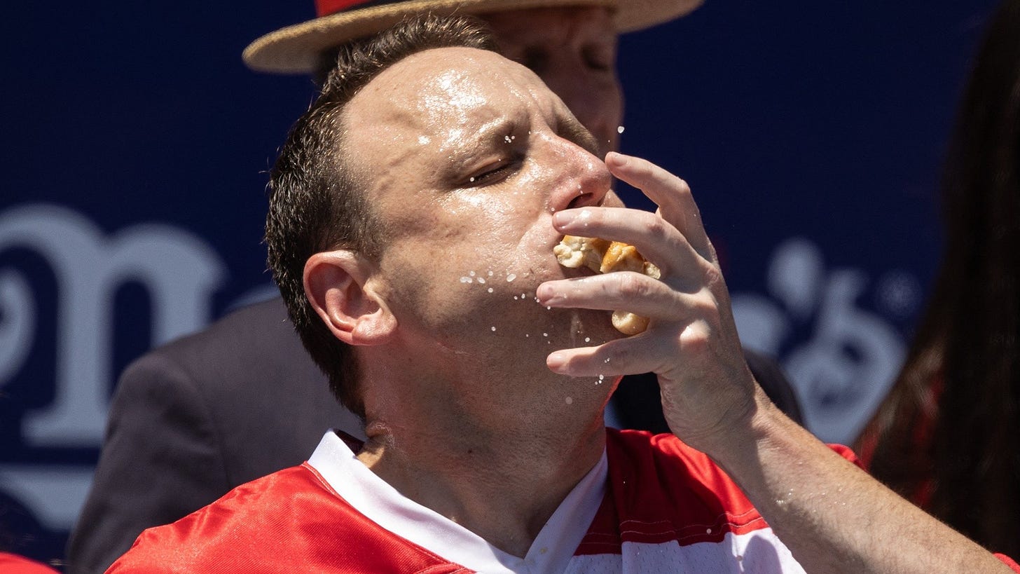 Joey Chestnut stuffing hot dogs into his face, sweating, cheeks are full