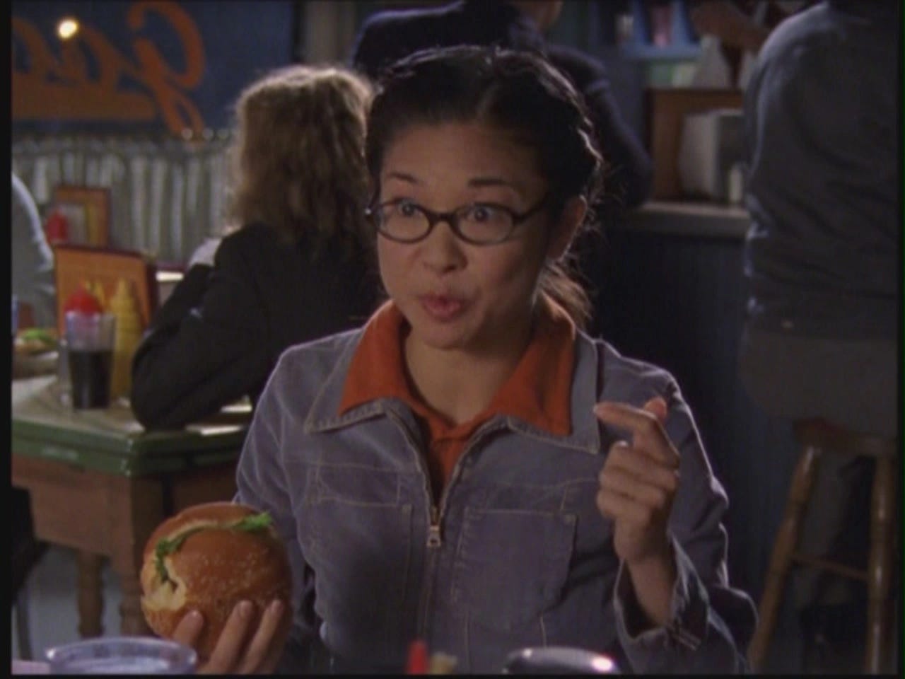 Lane Kim sitting in Luke's Diner and holding a burger. 