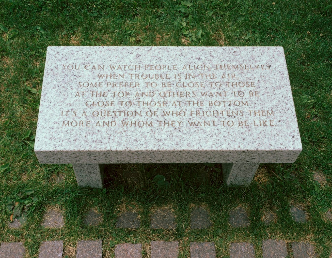 A small grey marble bench sitting outside is engraved with the words from the title.