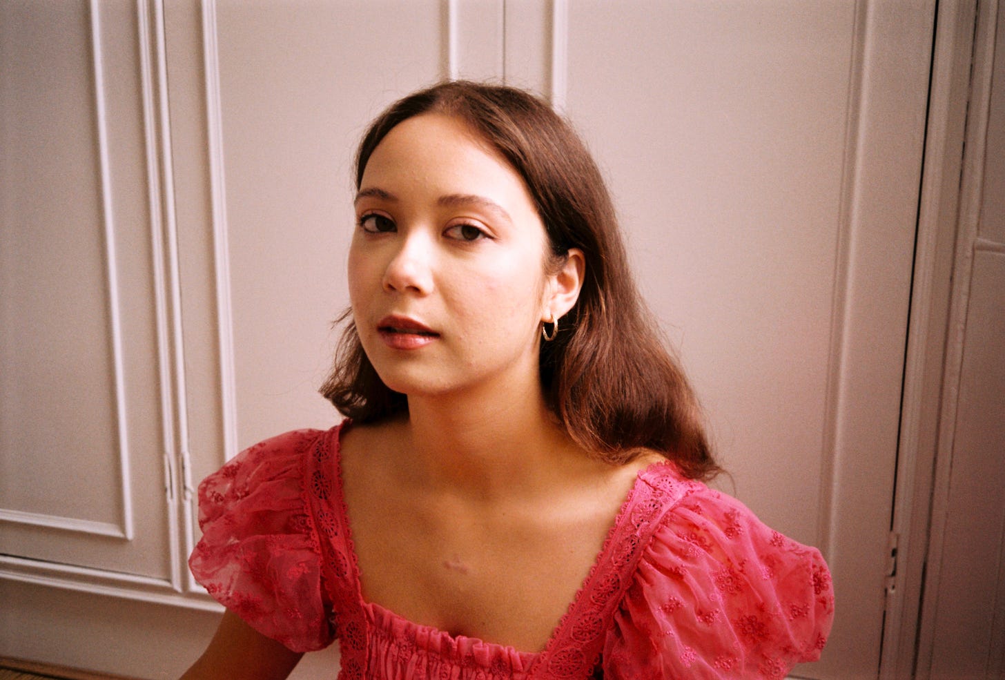 Junia photographed against a white background wearing a pink top with puffy sleeves