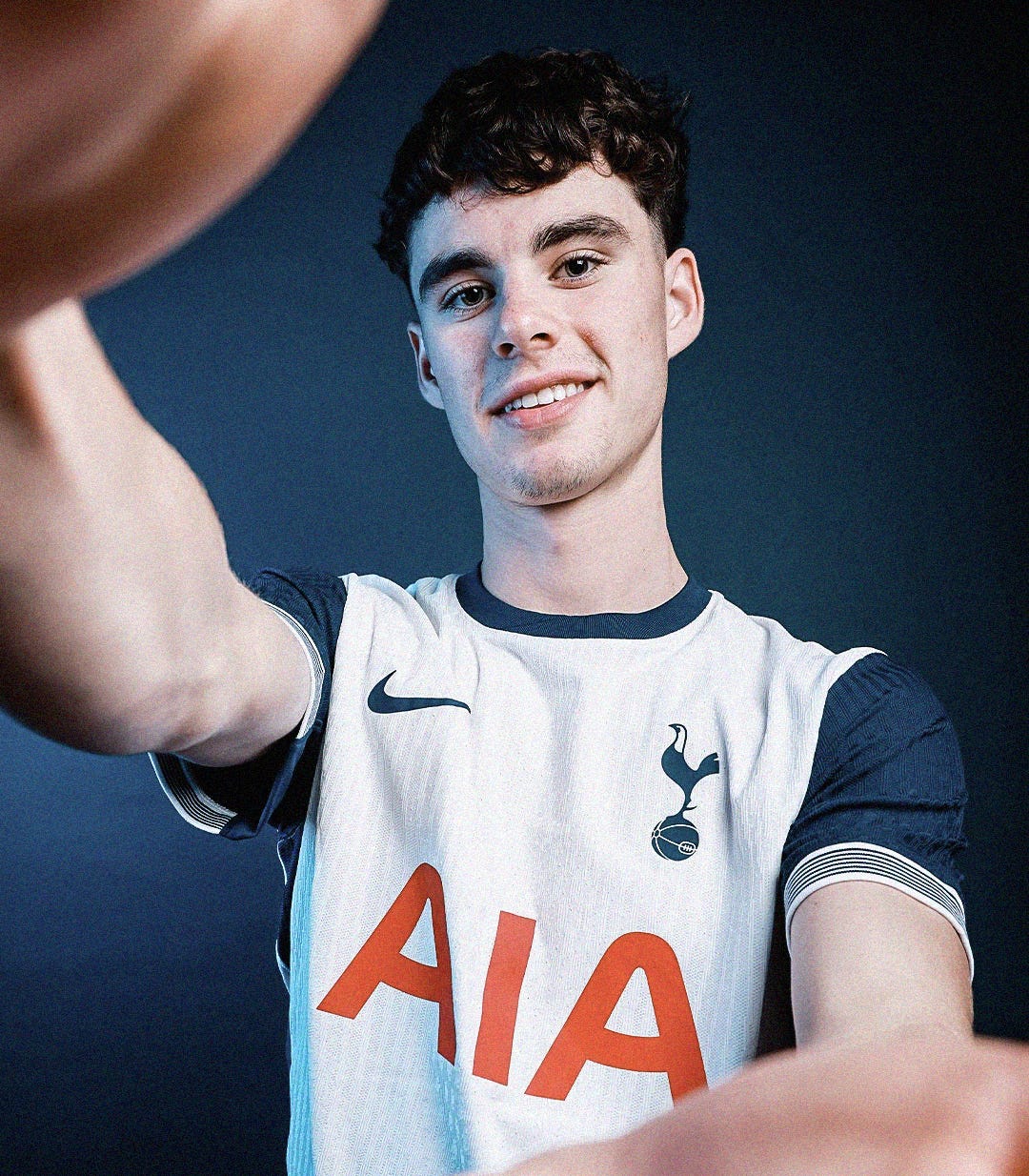 A close-up photo of Archie Gray in a white Tottenham Hotspur shirt with navy sleeves. He's stood against a navy backdrop.