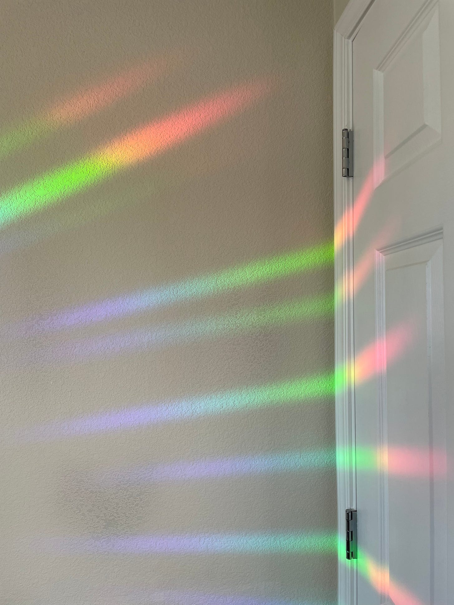 Rays of rainbow-colored light shown against a white wall and door. 