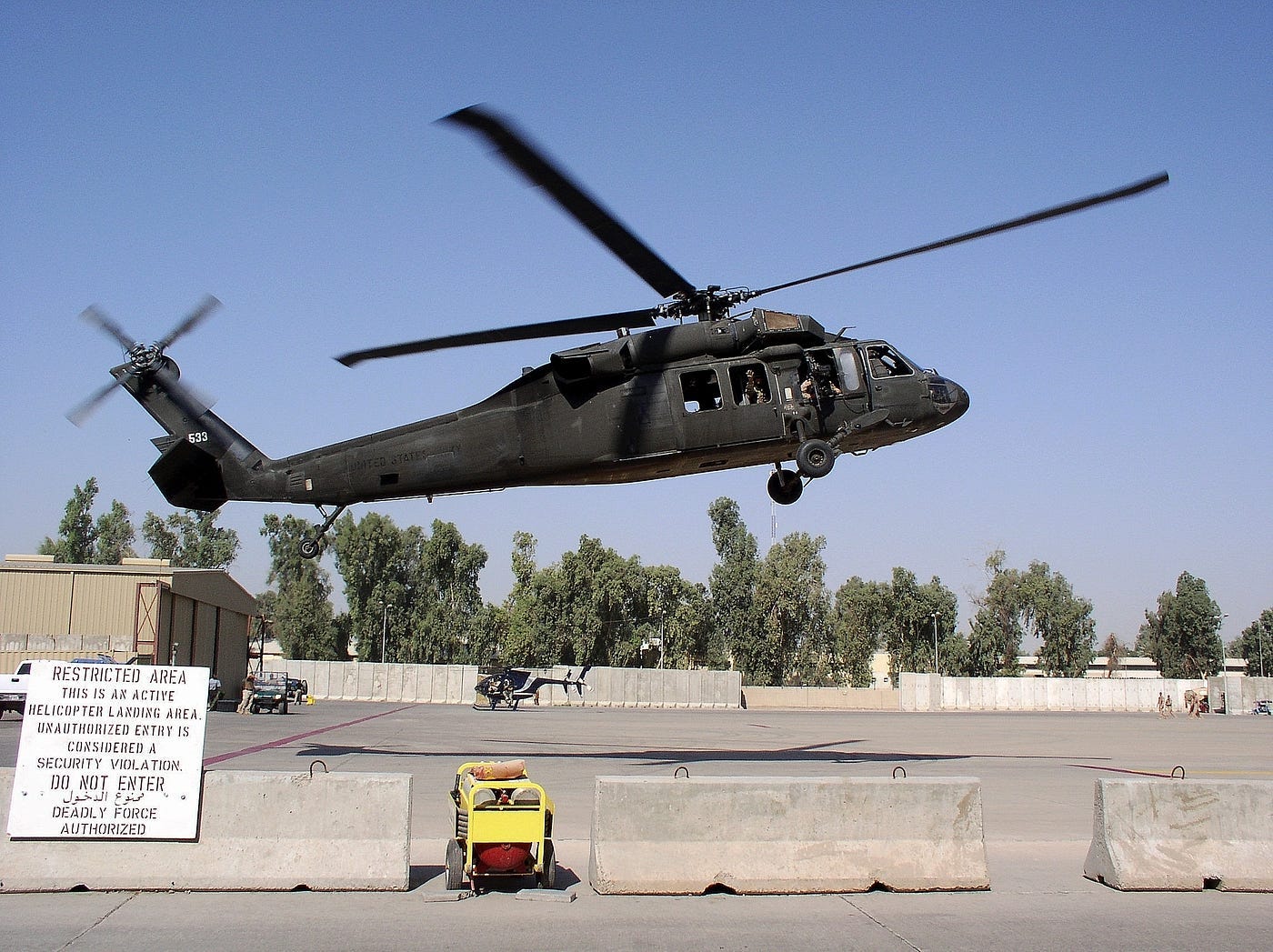 Blackhawk helicopter taking off from an American air base, sign warns of danger in both English and Arabic
