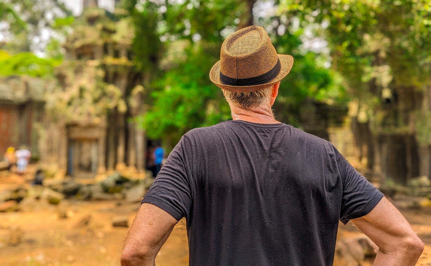 Michael wearing a brown straw hat and seen from behind as he looks at some ruins of Angkor Wat.