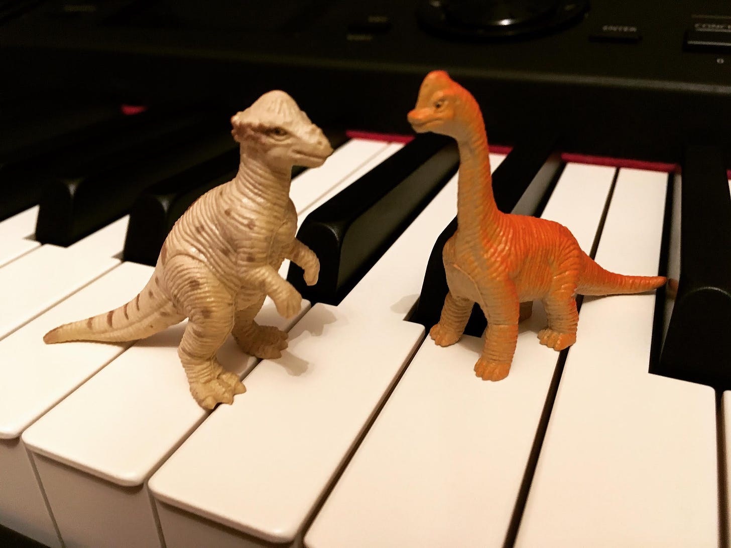 A very small brachiosaurus and an equally sized pachycephalosaurus standing on a piano keyboard.