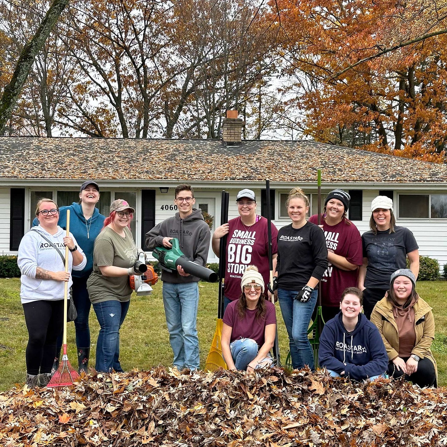 A group of Roastar employees pose behind a pile of leaves in front of a white ranch home covered in leaves from the surrounding oak and maple trees.