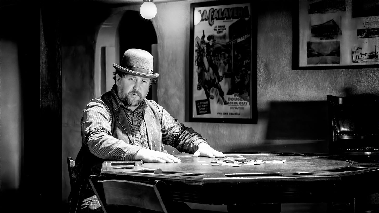 A black and white photo of a man wearing a bowler hat seated at a card table.