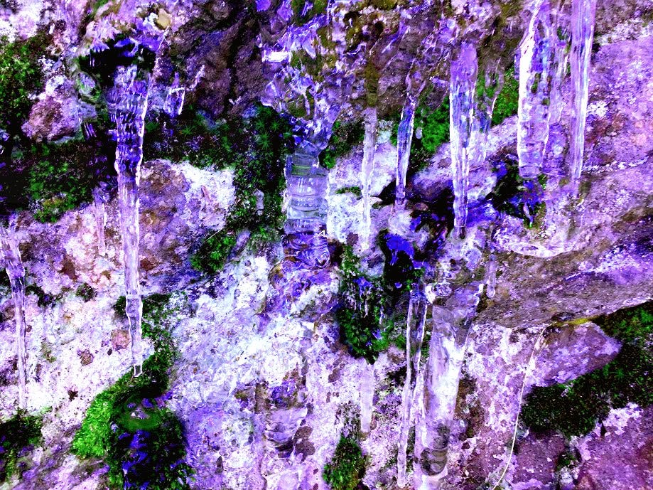 Close-up image of icicles on a mountain wall. The image has a bright purple hue.